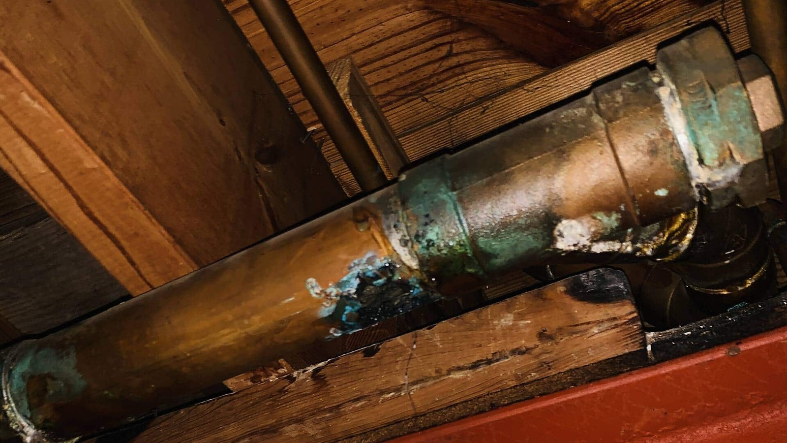 Corroded burst copper pipe above damaged ceiling materials, illustrating a cause of indoor water damage