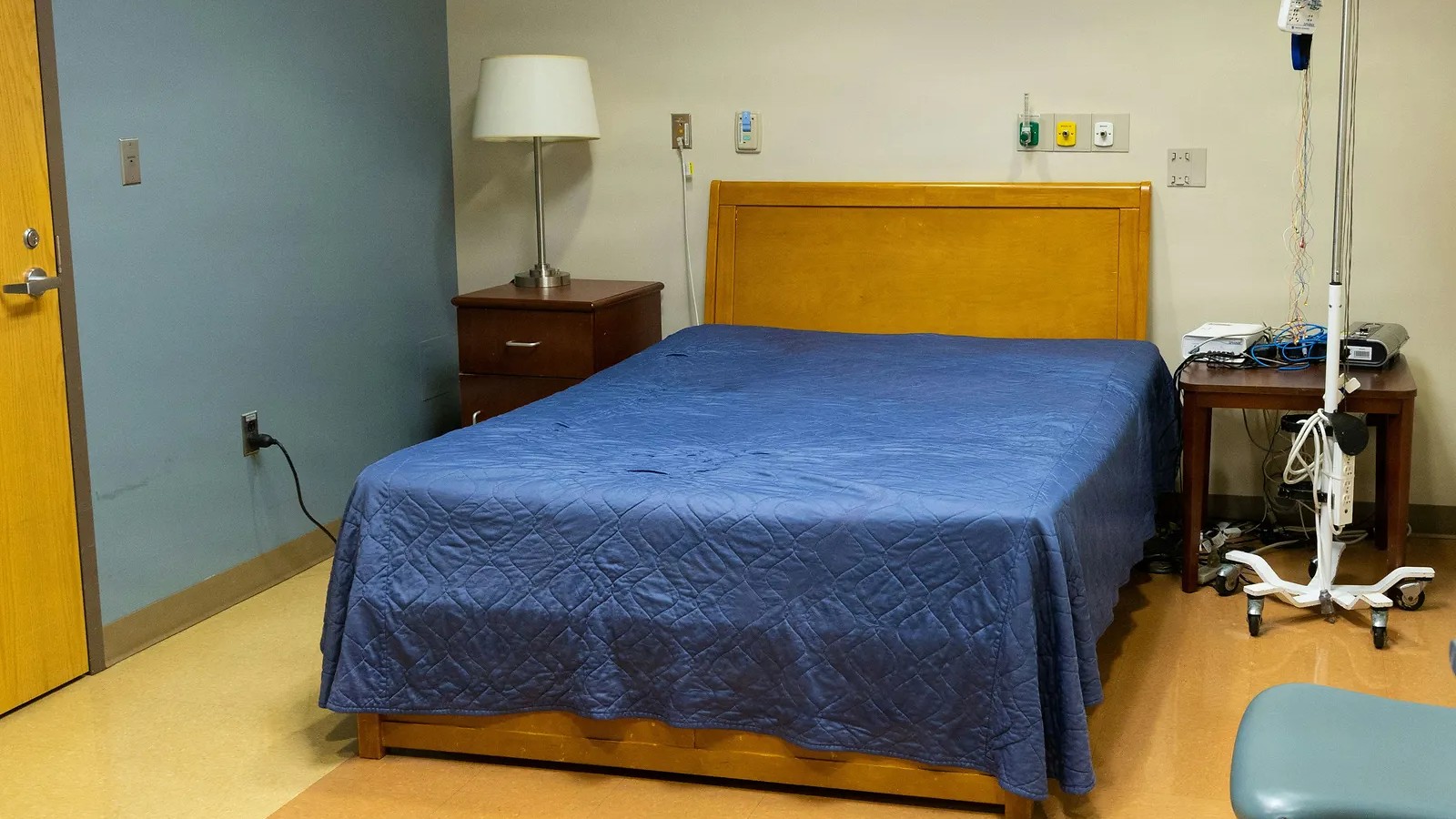 Empty medical patient room with a made bed, clean flooring and an IV stand