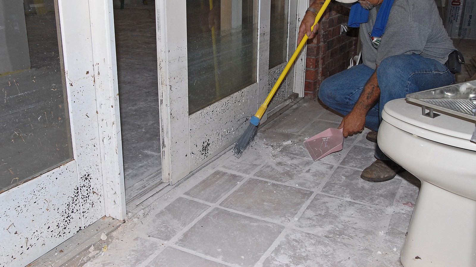 Flood cleanup: a worker sweeping mud and residue from a flood-damaged indoor tiled floor